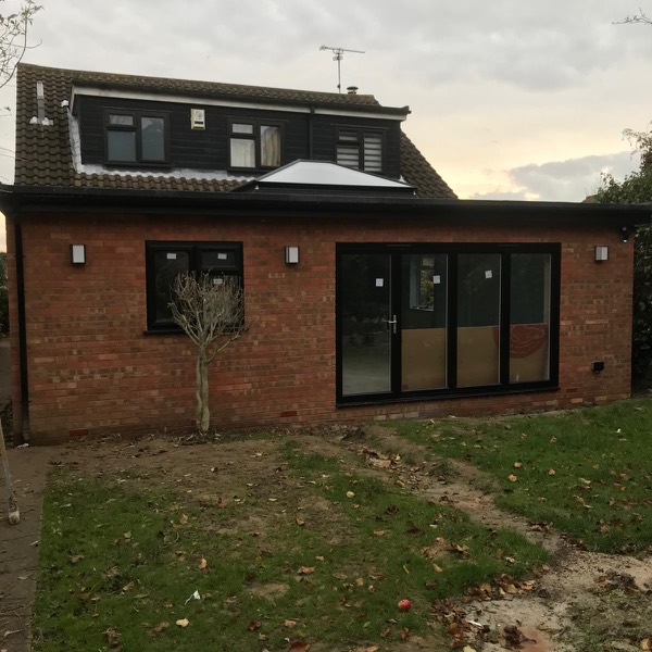 Single storey brick extension with black bi-folds and a roof lantern at dusk