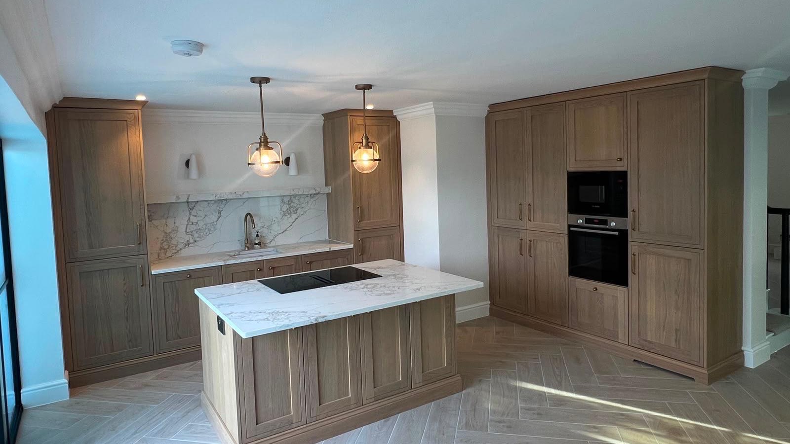 Oak shaker kitchen with a hob island, marble-effect worktops and brass pendant lights