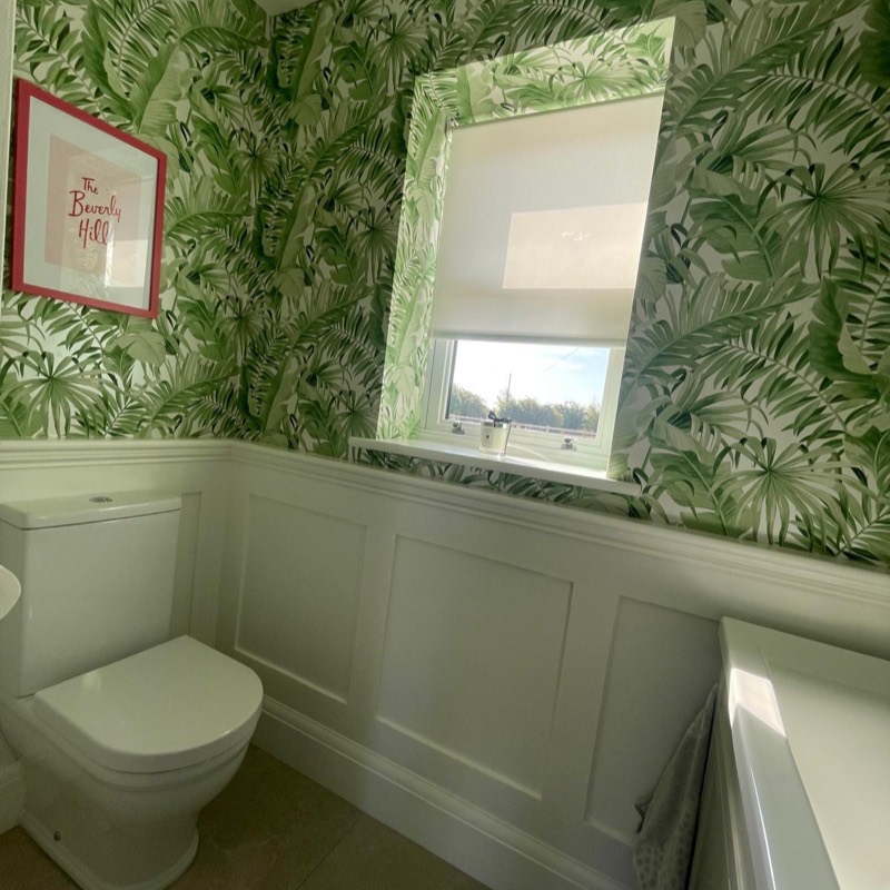 Palm print feature wallpaper above white wall panelling, with a toilet and bath