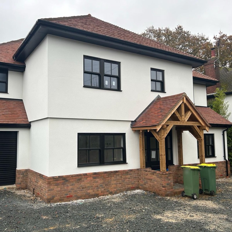 White rendered detached house with clay tiles, black sash windows and an oak framed porch