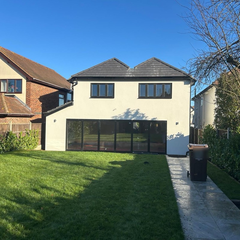 Back of a white rendered house with bi-fold doors opening onto a new lawn